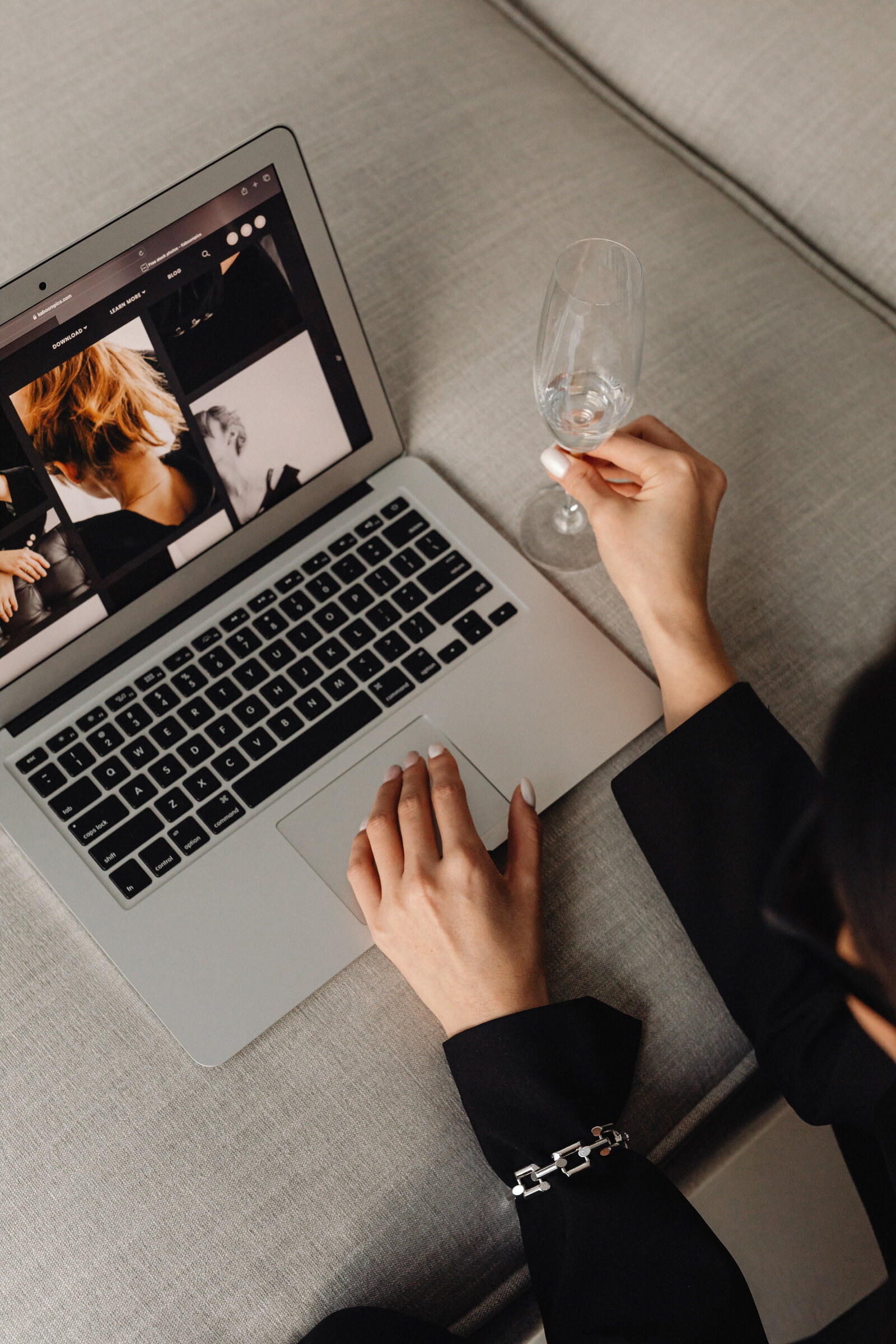 Person using a laptop on a couch, browsing photos of people, while holding an empty wine glass in one hand. Inner North Bookkeeping
