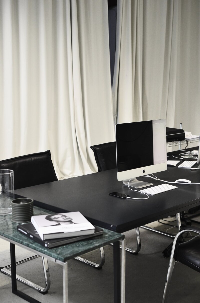 A modern office workspace with two computers on a black table, black chairs, a green side table, stacked books, and white curtains in the background—ideal for a BAS agent Melbourne professional managing finances using a BAS calculator or completing a BAS worksheet. Inner North Bookkeeping